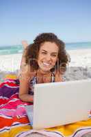 Young smiling woman typing on her laptop while lying on the beac