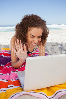 Young woman waving her hand in front of her laptop while lying o