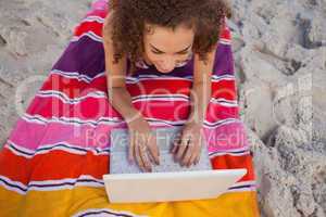 Overhead view of a young woman using her laptop on her beach tow