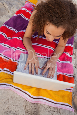 Young smiling woman lying on her beach towel while typing on her