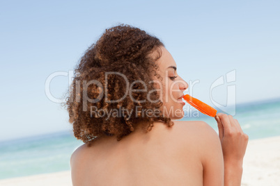 Attractive young brunette eating an orange ice lolly in front of