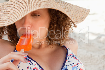 Relaxed young woman wearing a straw hat while eating an ice loll