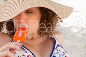 Relaxed young woman wearing a straw hat while eating an ice loll