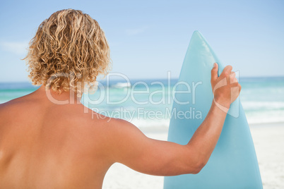 A young blonde man holding a perched surfboard