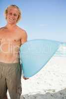 Young smiling man holding his blue surfboard