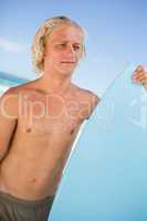 Young attractive man holding his perched surfboard in front of t