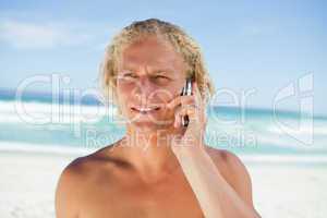 Blonde man talking on his mobile phone while standing on the bea