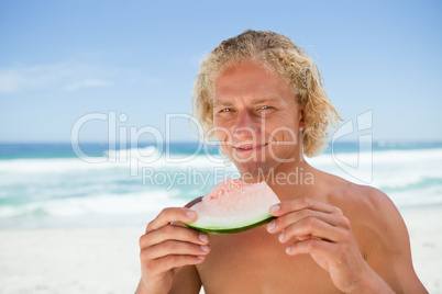 Smiling blonde man holding a piece of a watermelon while standin