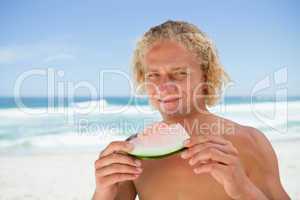Smiling blonde man holding a piece of a watermelon while standin