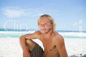 Serious man sitting on the beach while looking towards the side