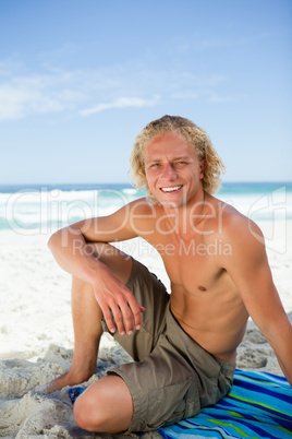 Smiling man sitting on his beach towel while looking at the came