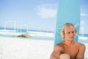 Blonde man sitting in front of his surfboard while looking towar