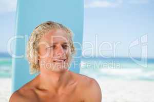 Smiling young man sitting on the beach with his surfboard