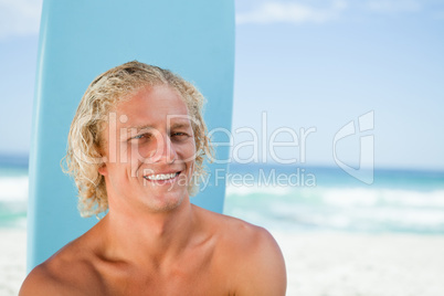 Smiling young man sitting in front of the ocean with his surfboa