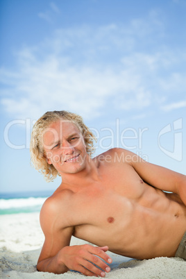 Young smiling man lying on the beach while looking at the camera