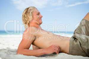 Side view of a blonde man lying on the beach