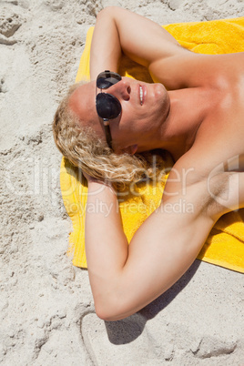 Young blonde man wearing sunglasses while lying on his yellow be