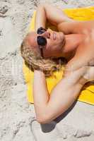 Young blonde man wearing sunglasses while lying on his yellow be