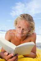 Serious man lying on his beach towel while reading a book