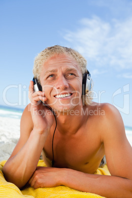 Smiling man lying on the beach while listening to music