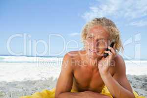 Young blonde man lying on the beach while talking on the phone