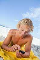 Young blonde man sending a text with his cellphone while sunbath