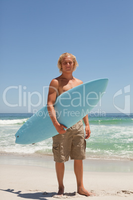 Blonde man holding his surfboard while standing in front of the