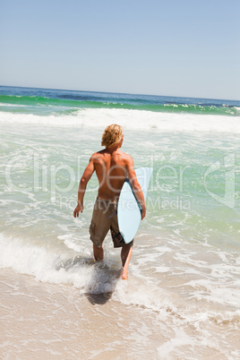 Young blonde man holding his surfboard while walking in the wate