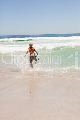 Young blonde man running in the water with his surfboard