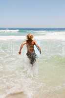 Young blonde man holding his blue surfboard while running in the
