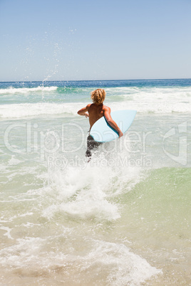 Blonde man running fast in the water while holding his surfboard