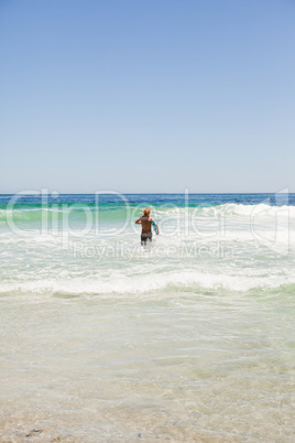 Rear view of a blonde man running in the water with his surfboar