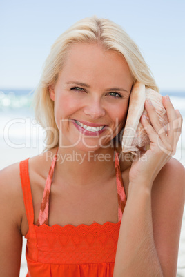 Young smiling woman holding a shell to hear the sound of the sea