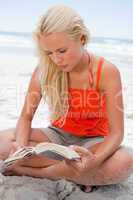 Young blonde woman sitting cross-legged while reading a book