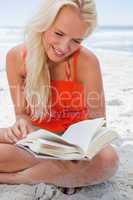 Young blonde woman reading a book while sitting cross-legged on