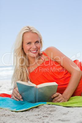 Smiling young woman lying on the side while reading a book