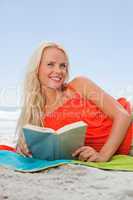 Young woman looking up while lying on her side and reading a boo