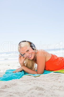 Young smiling woman lying on her beach towel while listening to