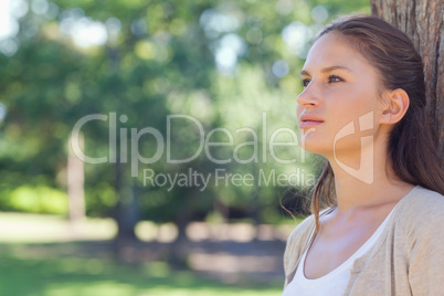 Woman standing with her back against a tree