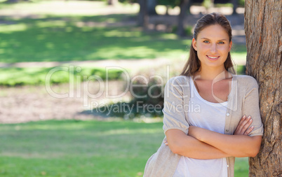 Smiling woman with her arms folded and leaning against a tree