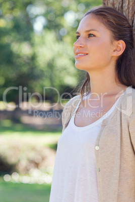 Smiling woman leaning against a tree in the park