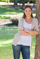Smiling woman with her arms crossed leaning against a tree