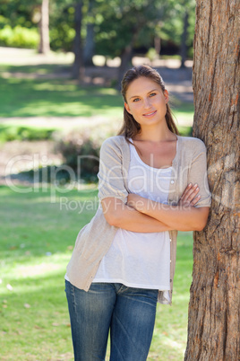 Smiling woman with her arms folded leaning against a tree