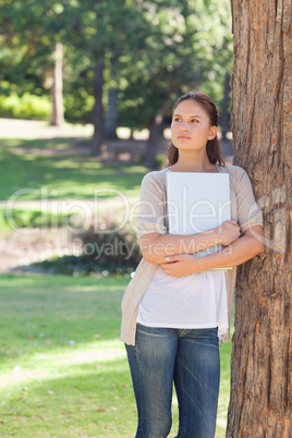 Woman with a laptop leaning against a tree