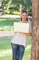 Woman using a laptop while leaning against a tree
