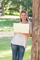 Smiling woman using a laptop while leaning against a tree