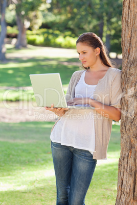 Woman using a notebook while leaning against a tree