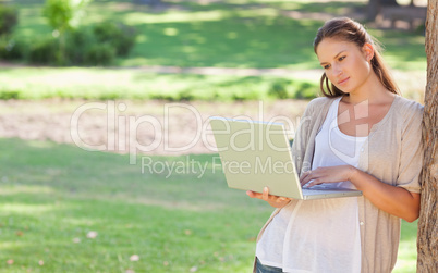 Woman leaning against a tree while using a laptop