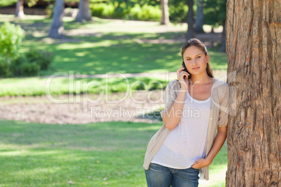 Woman on the phone leaning against a tree