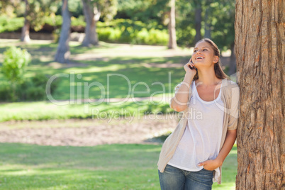 Cheerful woman on the phone leaning against a tree